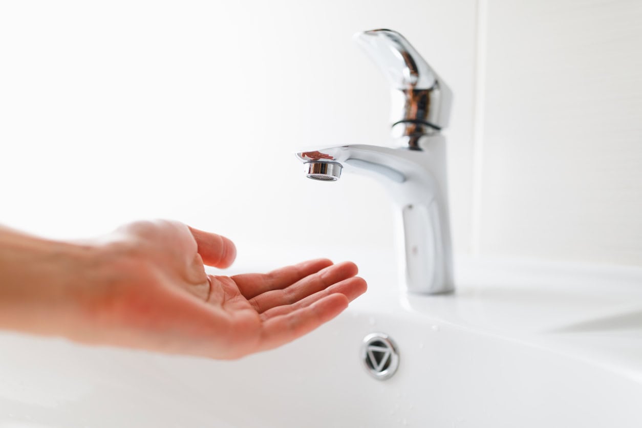 a person having their hand under a faucet without water