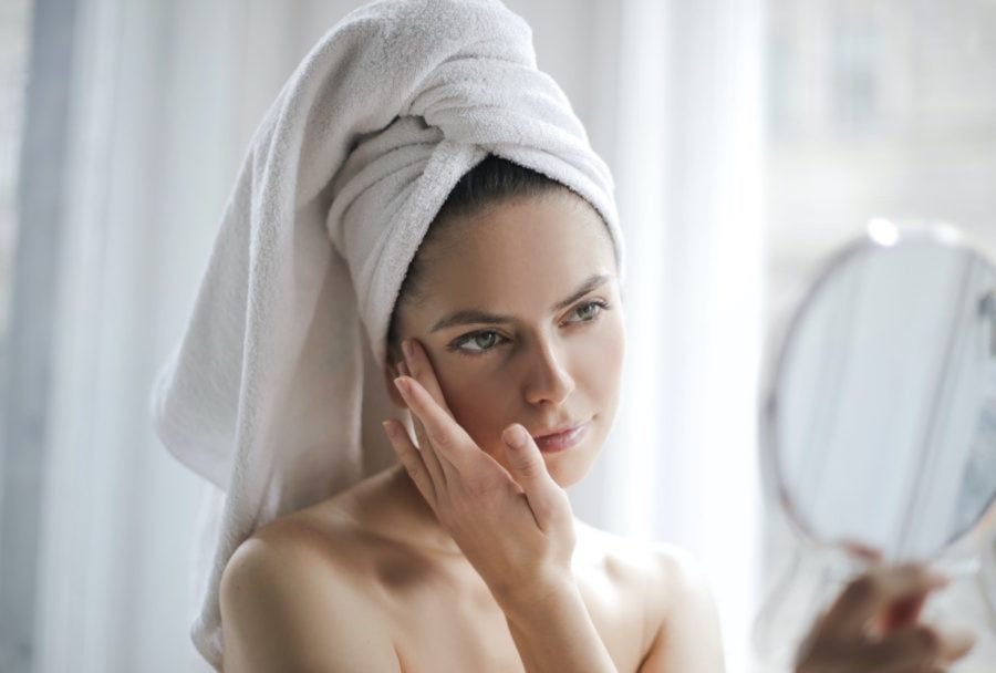 Woman checking mirror for signs of dry skin and hair from hard water