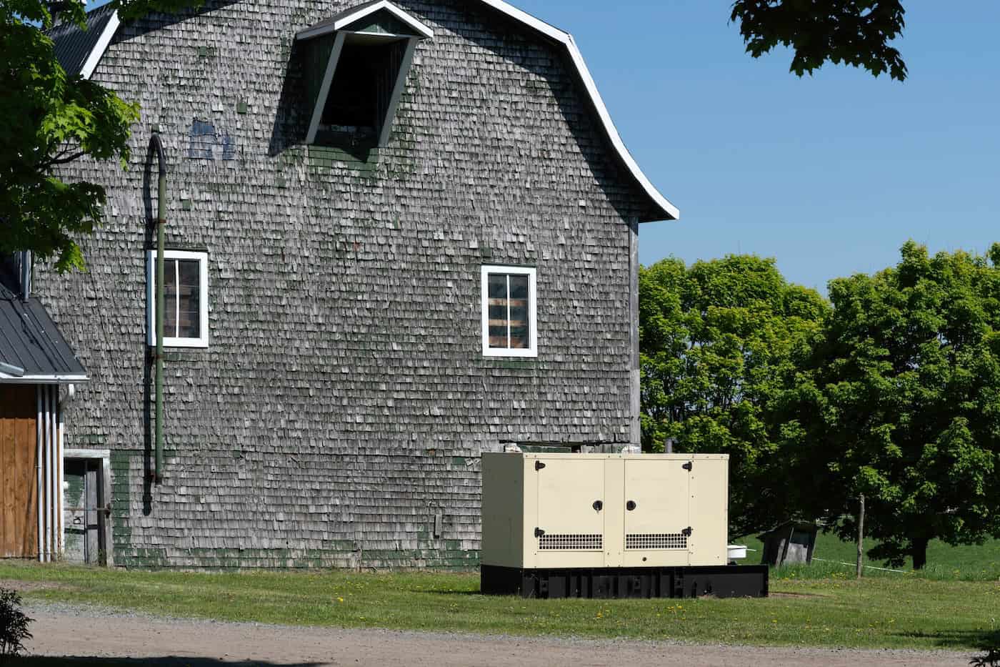 An Industrial Generator Near A Farm Building