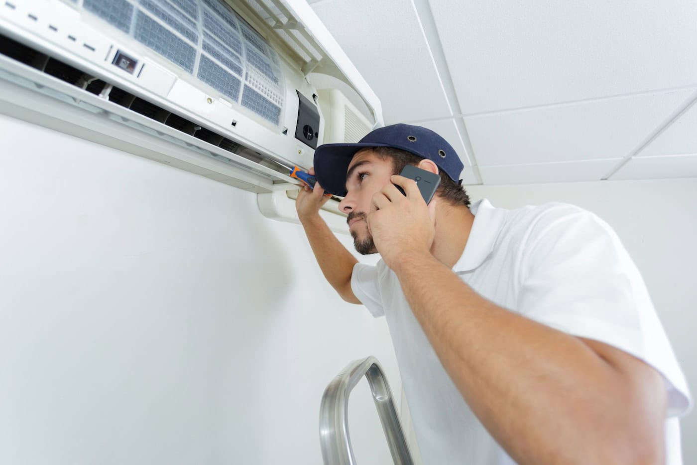 Young Handyman Repairing Air Conditioning System Calling For Help