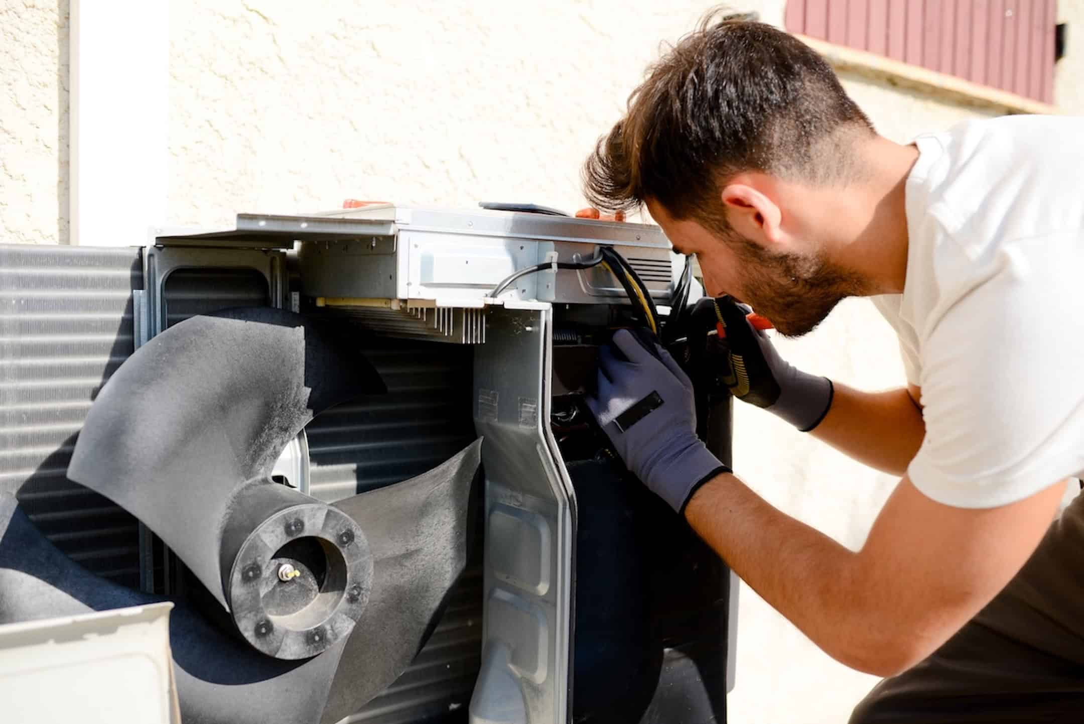 Young Man Electrician Installer Working On Outdoor Compressor Unit Air Conditioner At Client's Home