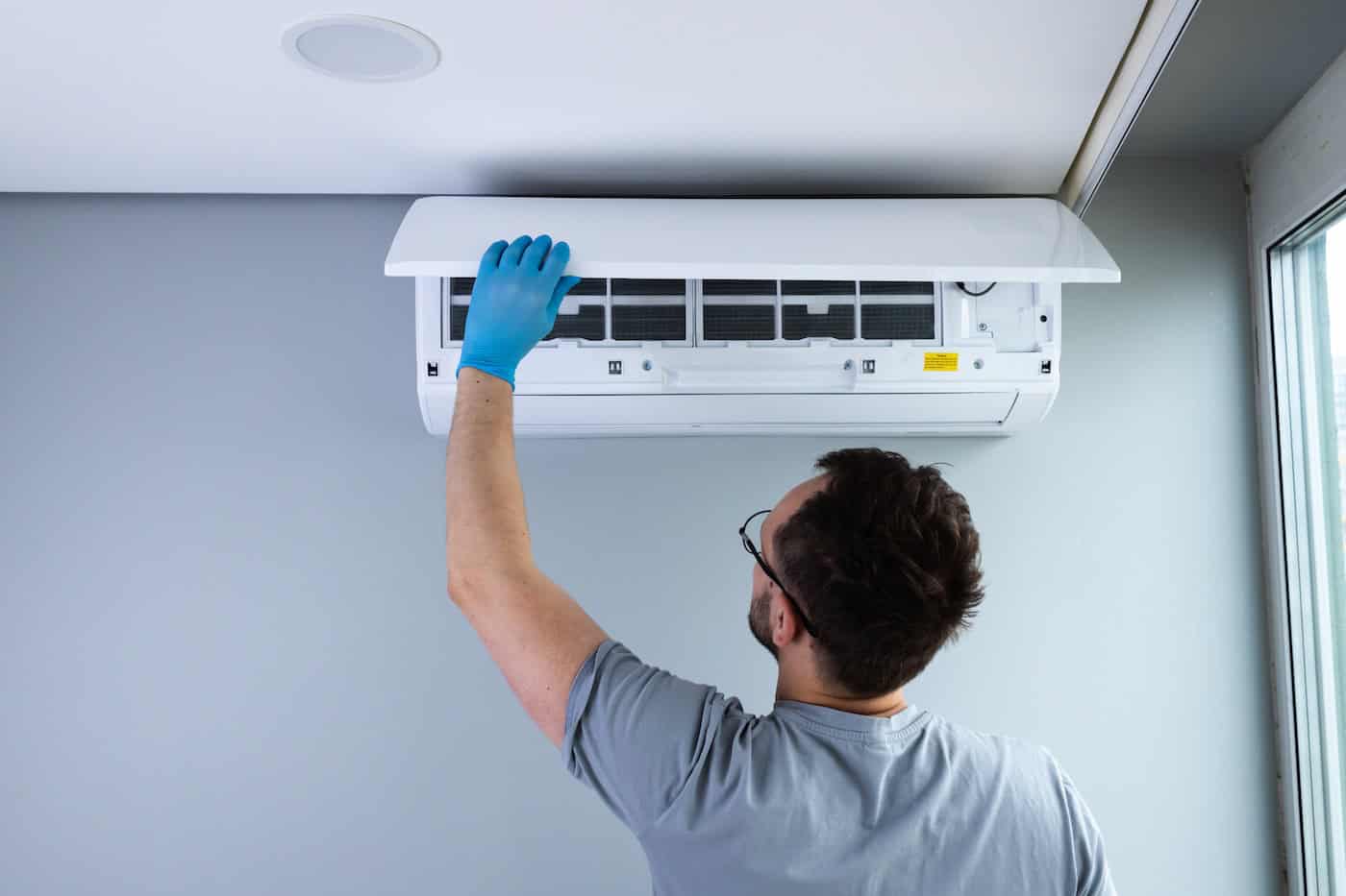 A Skilled Technician Performing Maintenance On A Ceiling Mounted Air Conditioning Unit With Focus On Cleanliness And Efficiency In A Contemporary Indoor Setting