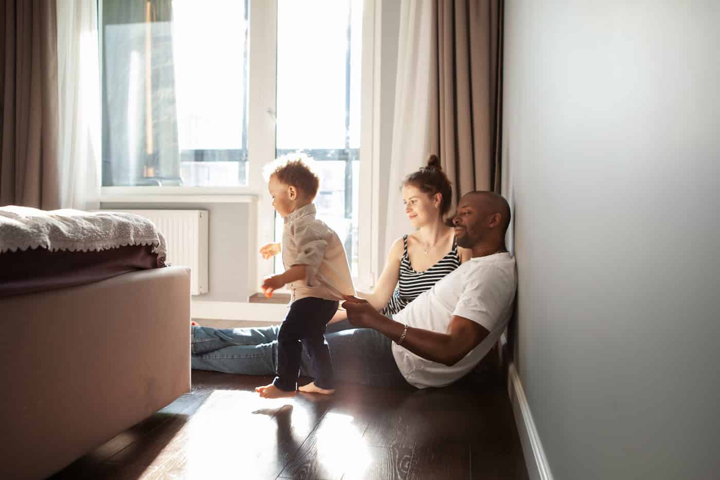 Family Playing With Child Son At Home, Authentic Family Life, Unposed, Spontaneous Moments. Baby Learning Walk And Dad Supports Him, Helps