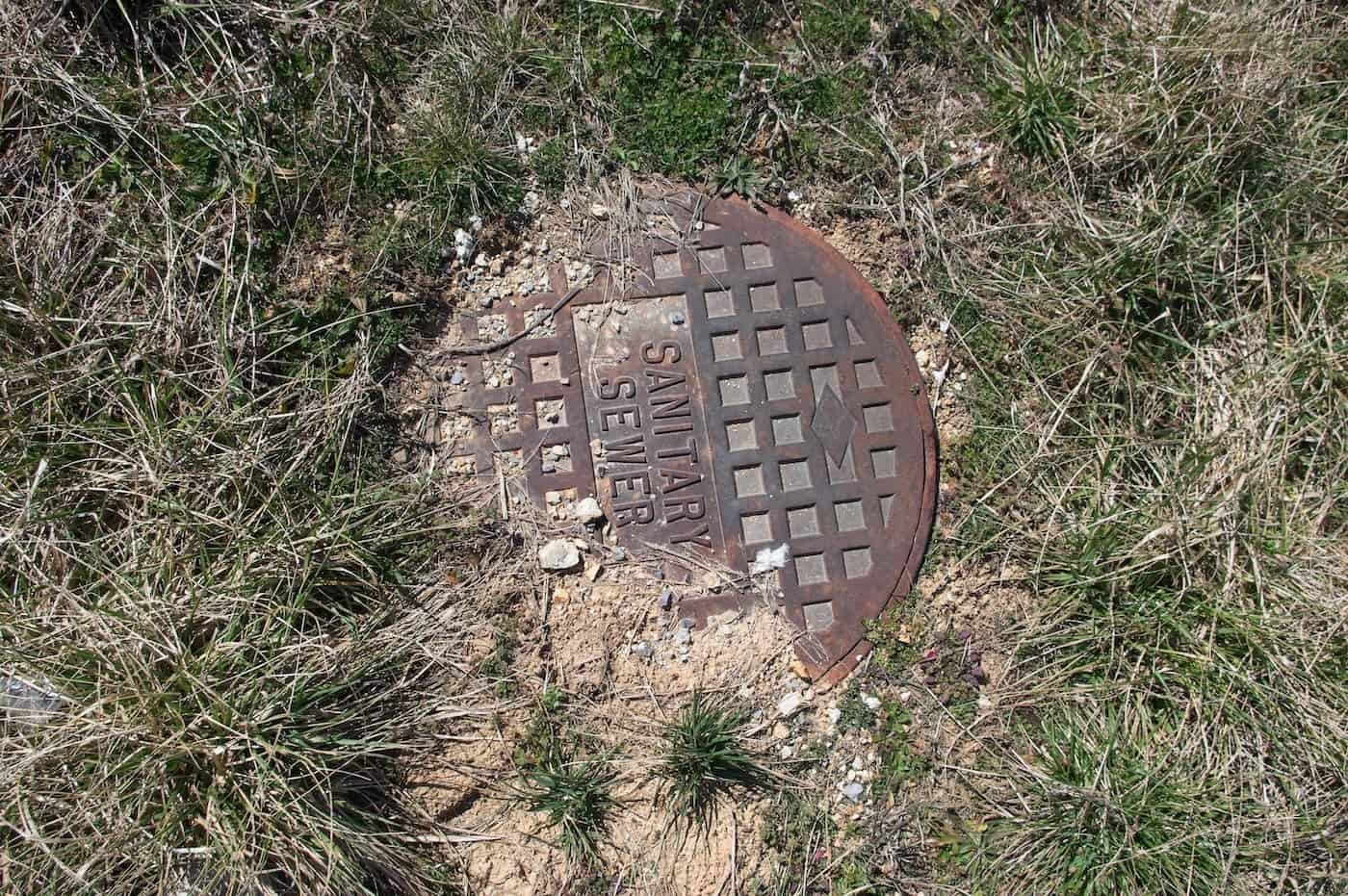 Iron Lid For A Sanitary Sewer With Grass And Dirt