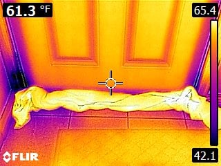 Thermal image of a door with a rolled-up cloth or towel placed along the bottom to block drafts; cooler temperatures are visible around the door edges, with the cloth warmer than the surrounding floor.