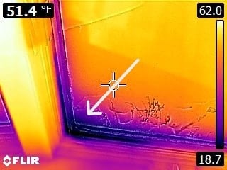 A thermal image of a window corner shows cool areas in purple and warm areas in yellow. A white arrow points to the bottom edge, indicating a temperature difference or possible air leak. Temperature readings are displayed.