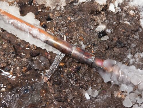 A 3/4" copper water main has frozen and cracked below ground outside a house. This is the line which runs from the street and services and individual house. In extreme cold this pipe can freeze and burst causing costly repairs. The background is excavated dirt.