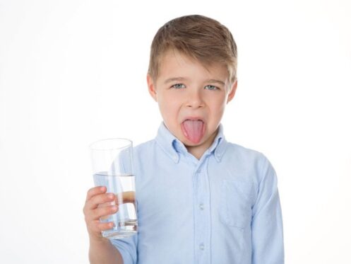 Kid sticking his tongue out because the water he is holding tastes bad