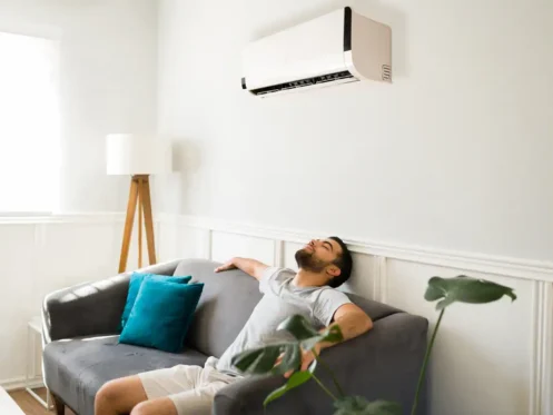 Man on a couch soaking in the cool air from an ac unit on the wall