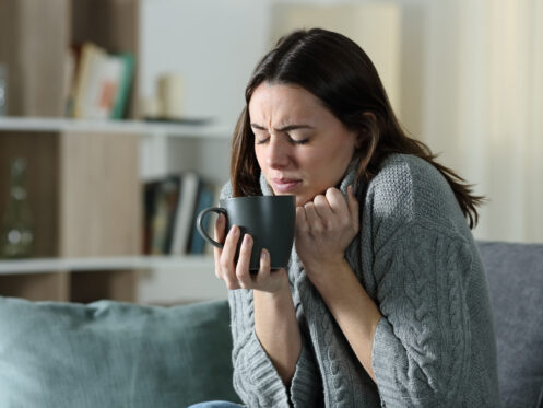 Cold woman bunched up holding a cup of coffee