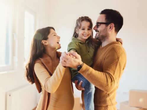 Happy pregnant family having fun while dancing together after moving into a new home.