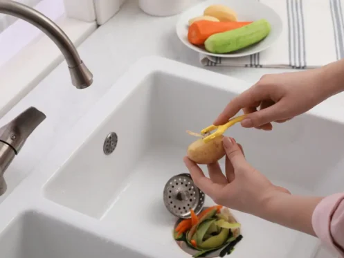 Person peeling vegetables into a sink with a garbage disposal